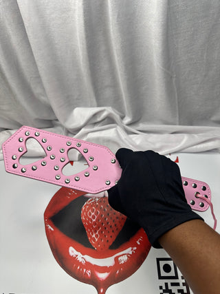 Pink leather paddle with heart-shaped cutouts and silver rivets displayed flat.