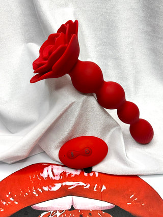 Rose Swirls red rotating anal plug with rose base displayed on INTAKE lips backdrop