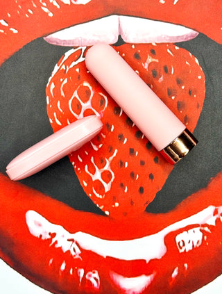 Flat lay of pink bullet vibrator and remote on red strawberry print background.