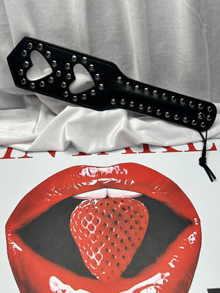Product shot of Love Taps paddle wrapped in black ribbon on red backdrop.