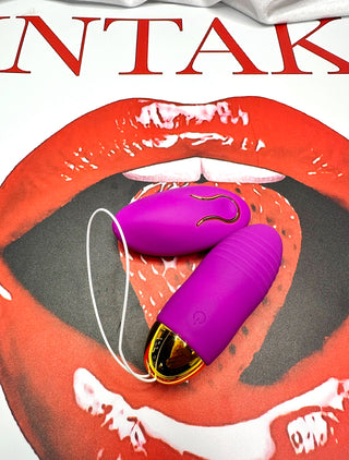 Purple remote control vibrator vibrating bullet laying on an INTAKE lips and strawberry background.
