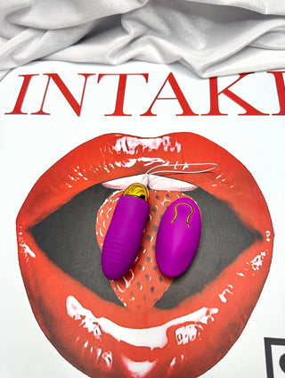 Wireless purple vibrating egg and matching remote positioned on the INTAKE strawberry lips artwork.