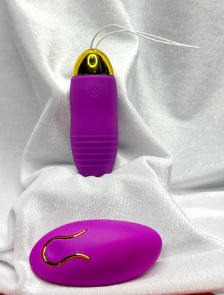 Purple wireless vibrating egg with gold accents displayed on white velvet fabric.