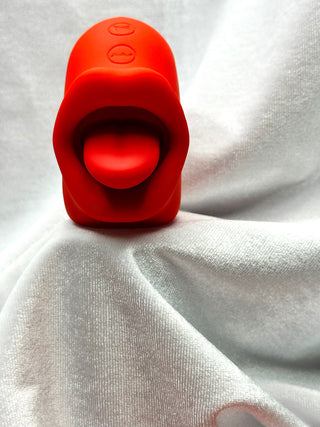 Tongue Kiss red silicone ring stimulator by INTAKE displayed on lips and strawberry backdrop.